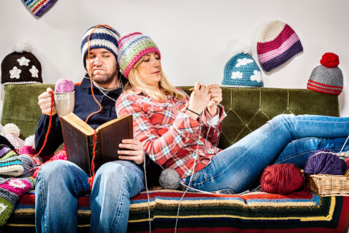 Annoying young knitter woman couple portrait on couch with winter hats