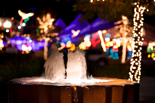 Water flows in fountain at night. Christmas lights visible in background in this urban, downtown district.