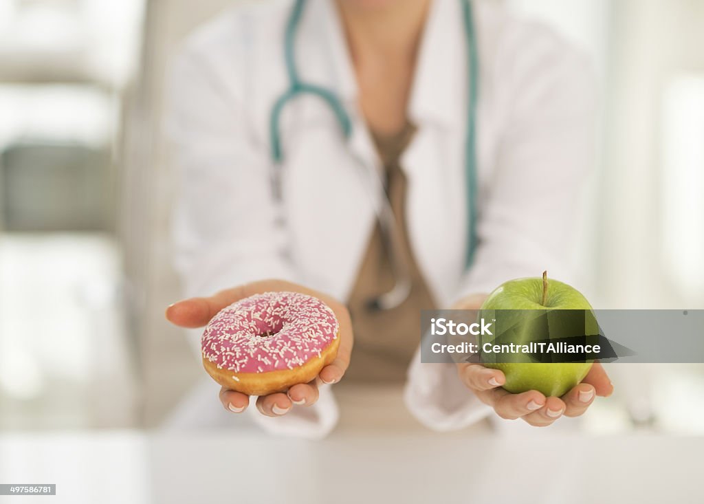 Closeup on doctor giving a choice between apple and donut Closeup on medical doctor woman giving a choice between apple and donut Diabetes Stock Photo