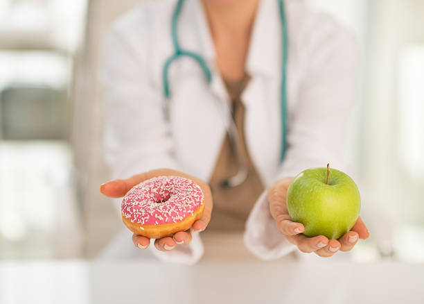 крупным планом на врач дает выбор между apple и пончик - diabetes food стоковые фото и изображения