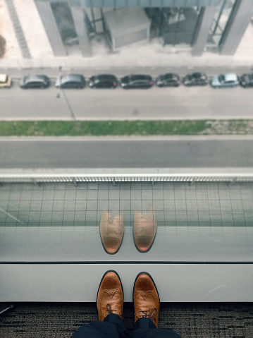 Businessman watching down from high level office. Focus on shoe.