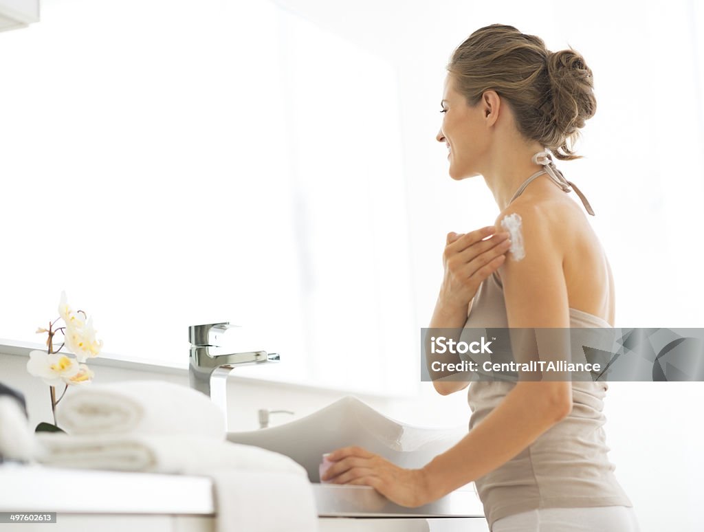 young woman applying cream on shoulder in bathroom Young woman applying cream on shoulder in bathroom Adult Stock Photo