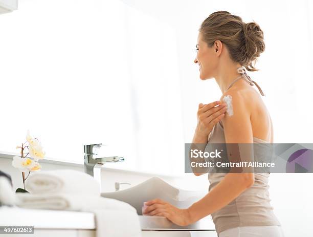 Young Woman Applying Cream On Shoulder In Bathroom Stock Photo - Download Image Now - Adult, Applying, Bathroom