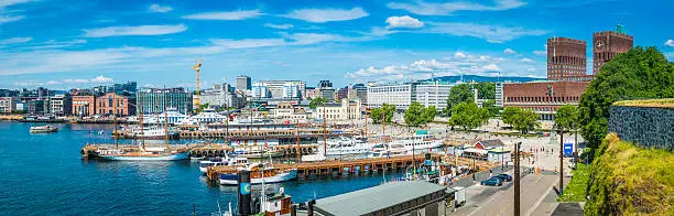 Panoramic vista across the busy waterfront of central Oslo, Norway's vibrant capital city, from the modern redevelopment of Aker Brygge to the broad promenade of Radhusplassen and the blue waters of Pipervika beside City Hall from the ramparts of Akershus fortress. ProPhoto RGB profile for maximum color fidelity and gamut.