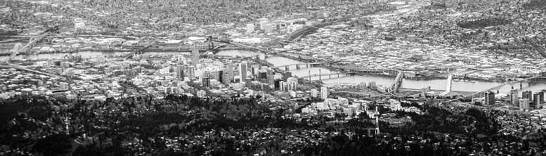 A wide panoramic letterbox view of downtown Portland, Oregon, the Willamette river stretching across the scene.   All of Portlands main bridges are visible in the picture (Broadway, Burnside, and Hawthorne to name a few).  Black and white image.