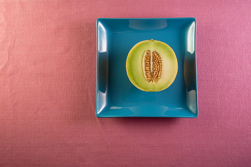 Cross section of Cantaloupe melon fruit on a blue plate and pink background