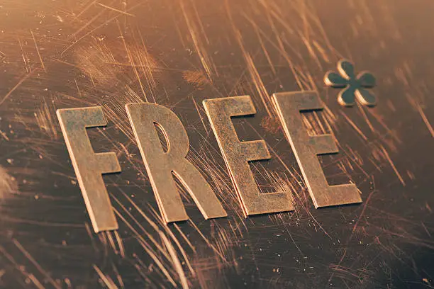 Cut copper letters forming the word âFreeâ with an Asterisk (fine print). Detail photo of metal letters
