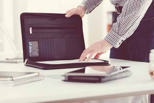Man taking documents from briefcase in an office. Close up of hands, unrecognizable person.