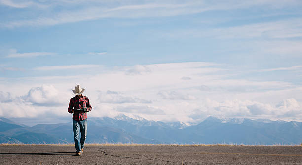 Western Man texts on cell phone while walking across rural highway