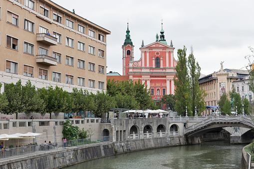 Bled, Slovenia - September 4, 2015: People walk along Ljubljanica River with Franciscan Church and Triple Bridge.