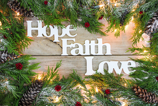 Christmas tree garland border with snow, lights, and the words Hope, Faith, Love on antique rustic wooden background