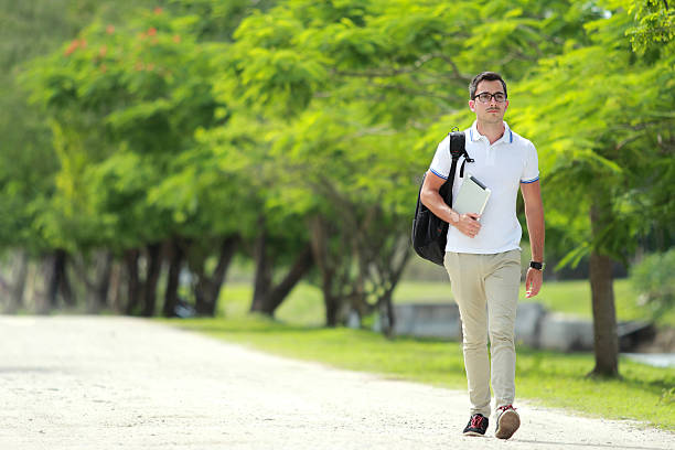 istock handsome college student walking by at park with backpack 497654058