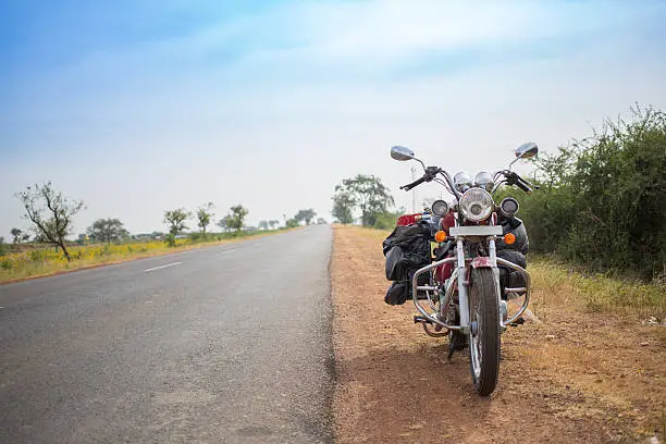 An image of a heavy packed motorcycle standing parked next to a long country road on a beautiful day.
