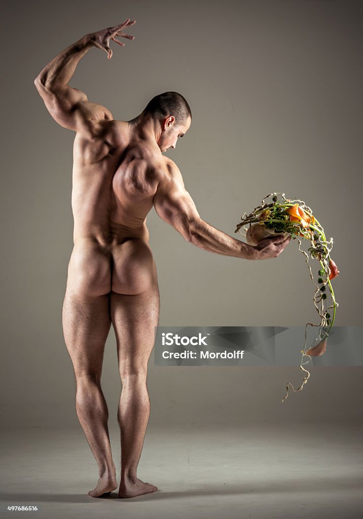 Hercules With Flower Arrangement Athletic nude young man posing  with a flower arrangement in your hand. He standing with his back and holding a bouquet of flower design on hand. Studio shooting Naked Stock Photo