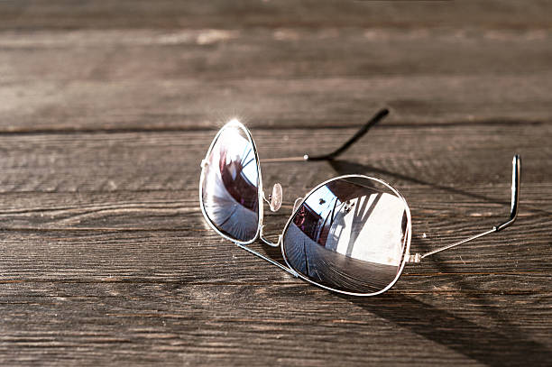 Metal thin trendy sunglasses on wooden table. Outdoors closeup. Metal thin trendy sunglasses on wooden table. Evening light.  Outdoors closeup. cool glasses hand colored sun stock pictures, royalty-free photos & images