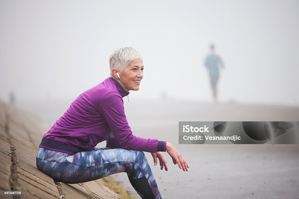 Morning jogging Beautiful mature woman jogging through fog in early autumn day Exercising Stock Photo