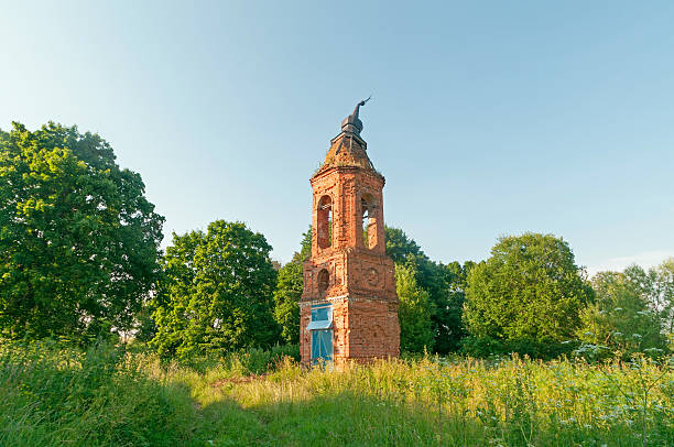 istock Old damaged brick belfry among trees against blue sky background 497689203