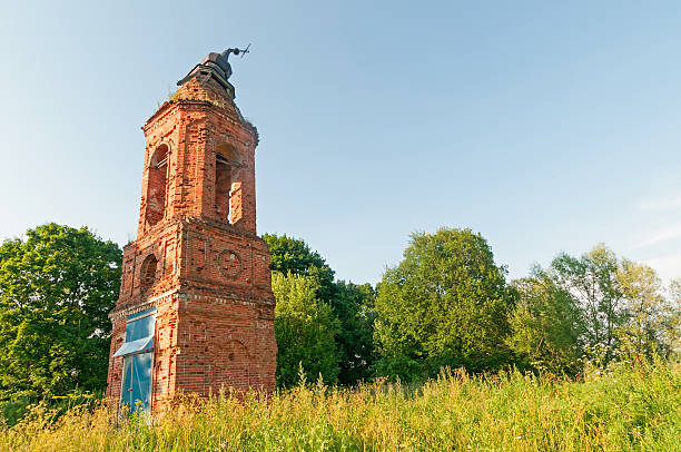 istock Old damaged brick belfry before trees against blue sky background 497689221