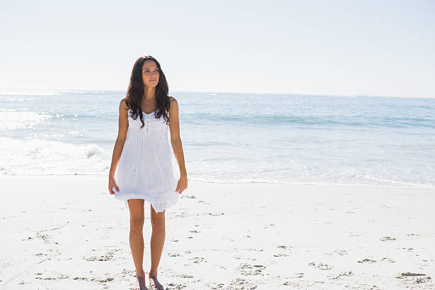 istock Happy brunette in white sun dress walking on the sand 497689629