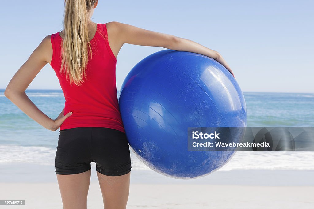 Fit blonde holding exercise ball looking at sea Fit blonde holding exercise ball looking at sea on the beach Fitness Ball Stock Photo