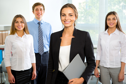 Happy female CEO with crossed arms looking at camera while her colleagues are in the background.