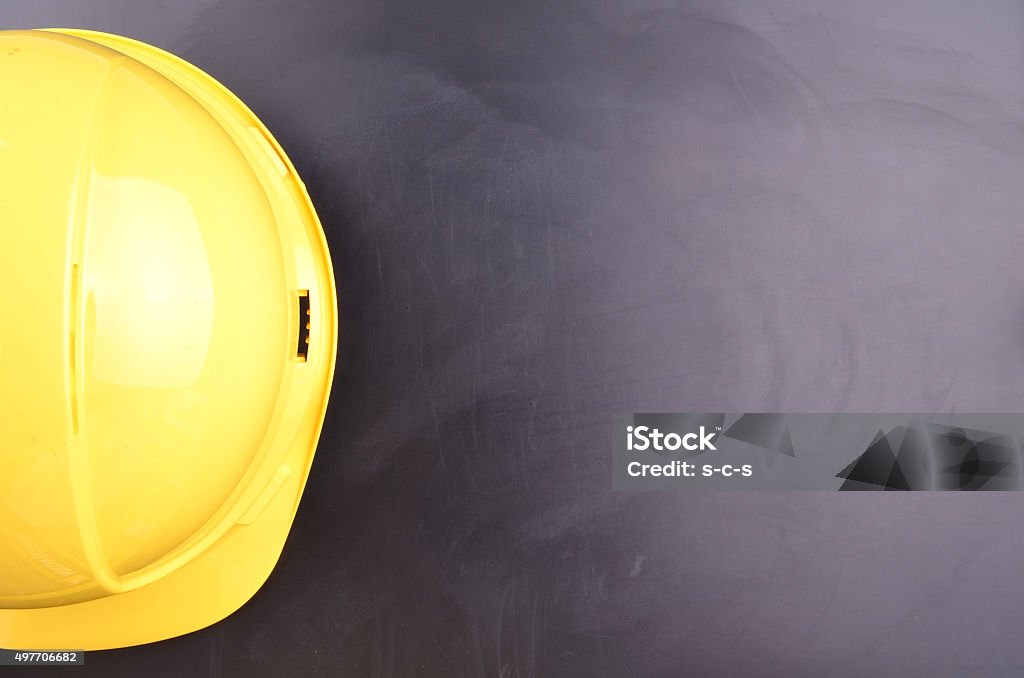 Work Place Safety Concept A yellow hard had hangs in front of a blackboard with blank scape to write text. Occupational Safety And Health Stock Photo