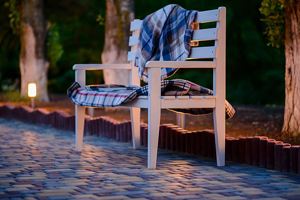 Inviting White Bench Covered in Plaid Blankets on Stone Patio Illuminated in Soft Light at Dusk