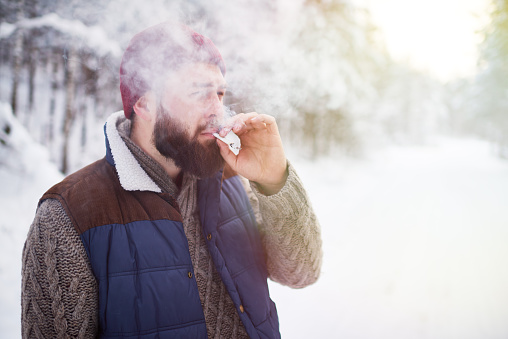 Frowning young man smoking in winter forest