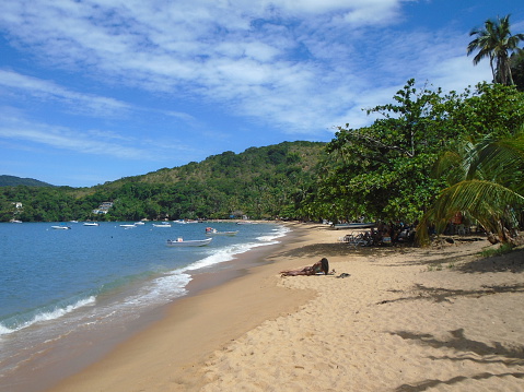 It's a sunny morning in Playa Hermosa, Costa Rica. Fishing boats are out in the bay on the calm water. It is dry season, and the surrounding dry forests have turned brown.