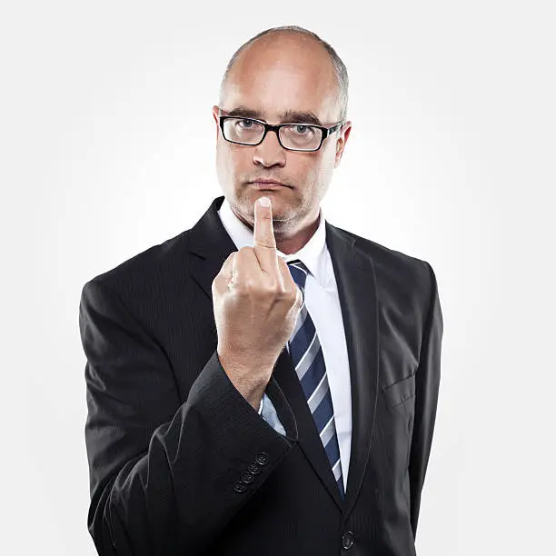 A serious looking middle-aged man with suit and necktie showing the middle finger. Selective focus