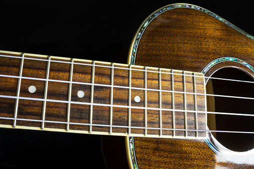 A close up photo of a beautiful Hawaiian Ukulele musical instrument with rich, dark brown wood grain textures.