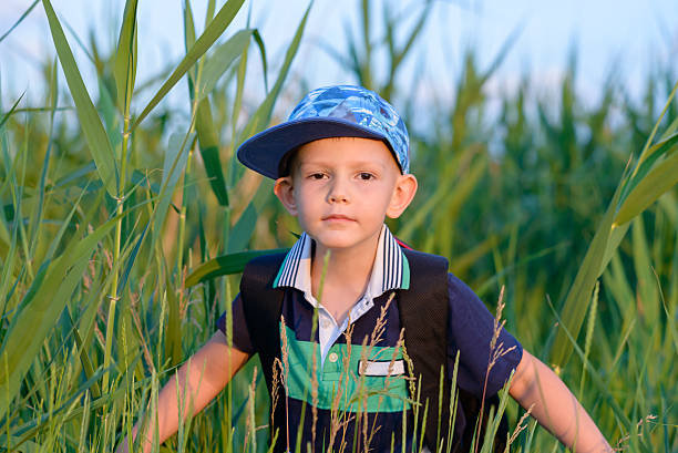 Young boy wearing a peaked cap hiding in fresh green reeds peering at the camera with a serious expression