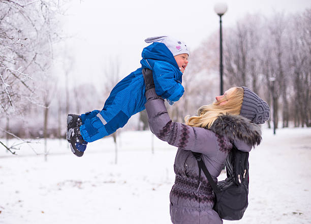 Happy mother and baby playing evergreen spruce in winter park stock photo