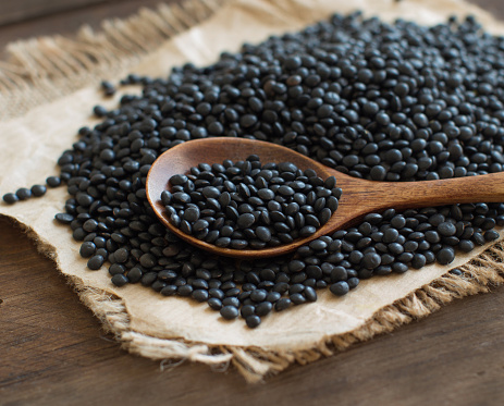 Black Lentils with a spoon on wooden table close up