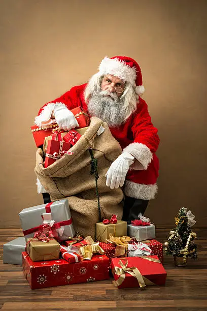 Photo of tired santa claus with many gifts in bag