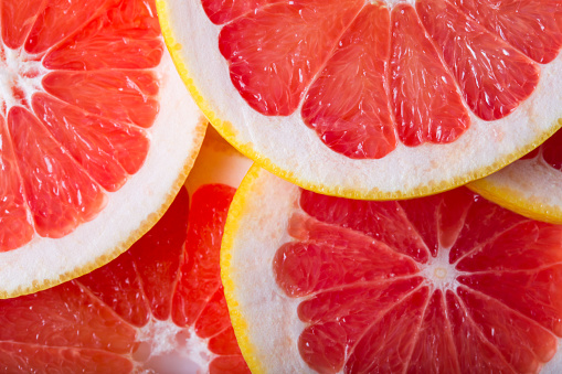 Stock photo showing close-up, elevated view of a row of citrus fruit slice wedges against a mottled grey background.