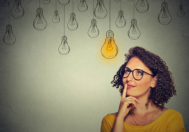 mujer con gafas mirando hacia arriba con idea de bombilla de luz - choice thinking women decisions fotografías e imágenes de stock