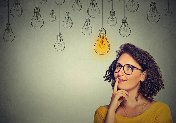 woman in glasses looking up with light idea bulb Portrait thinking woman in glasses looking up with light idea bulb above head isolated on gray wall background connect the dots photos stock pictures, royalty-free photos & images