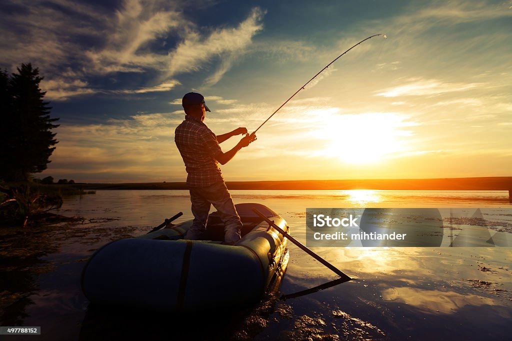 Fisherman in a pond Fisherman with rod in the boat on the calm pond at sunset Fishing Stock Photo