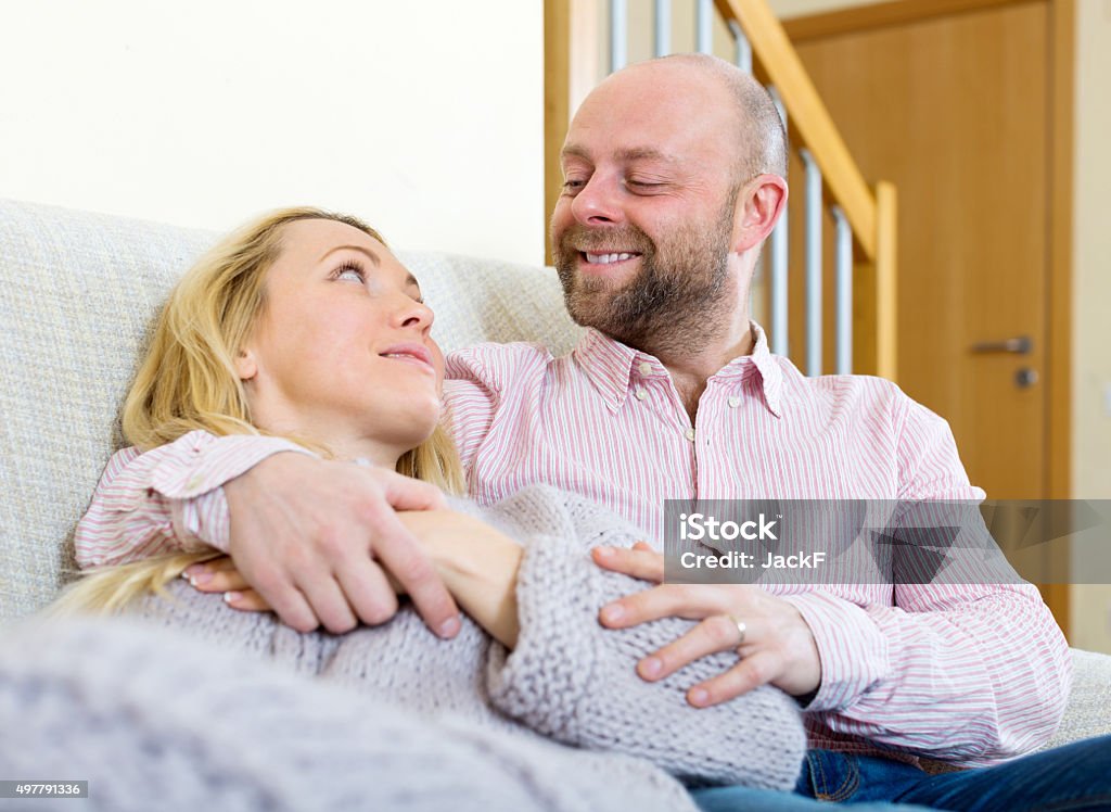 Loving couple  in home interior Adult couple in love at home in the living room sitting on sofa. Focus on man 2015 Stock Photo