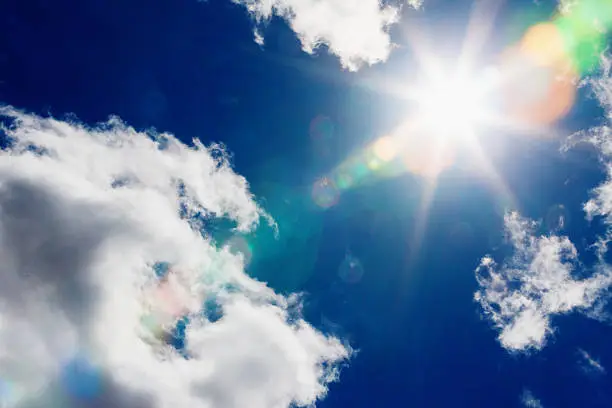Looking up at the sun, high in the sky and shining brightly with radiating lens flare effect in a slightly clouded sky.