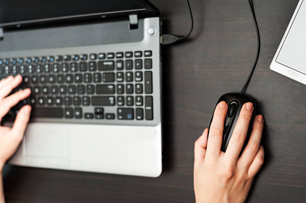 Working at the laptop computer in office top view Human hand on laptop computer keyboard and another hand controlling wired computer mouse at the desk and cell phone nearby. Top view. color image in horizontal orientation peoples alliance for democracy stock pictures, royalty-free photos & images