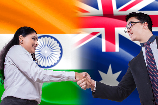 Image of young woman shaking hands with businessman in front of Indian and Australian flags
