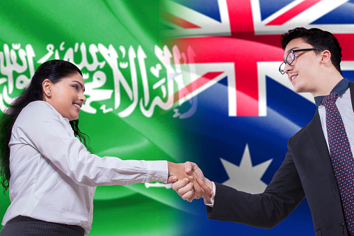 Photo of a young Australian businessman shaking hands with Arabian businesswoman in front of Australian and Arabian flags