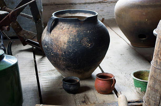Two old fashioned cups and a pitcher are hanging on a wooden board. The cups are white and blue, and the pitcher is blue with white spots. The scene has a vintage and rustic feel, with the cups
