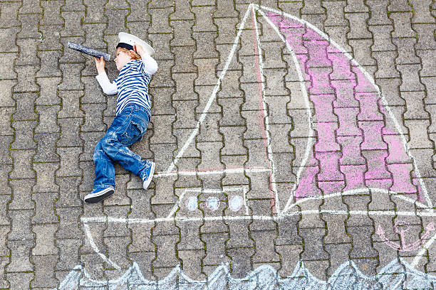 istock Little kid boy  with ship picture drawing with chalk 497811994