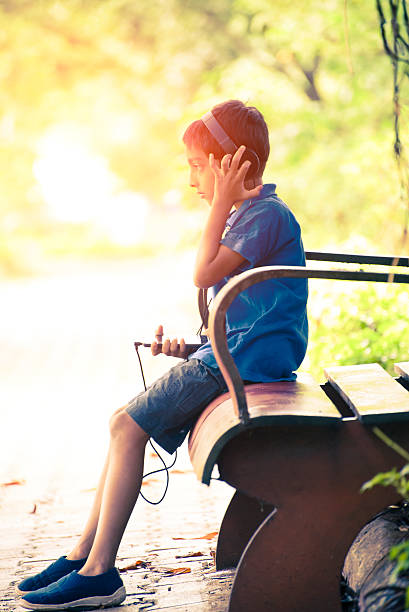 istock Boy listening to music on park bench 497813634