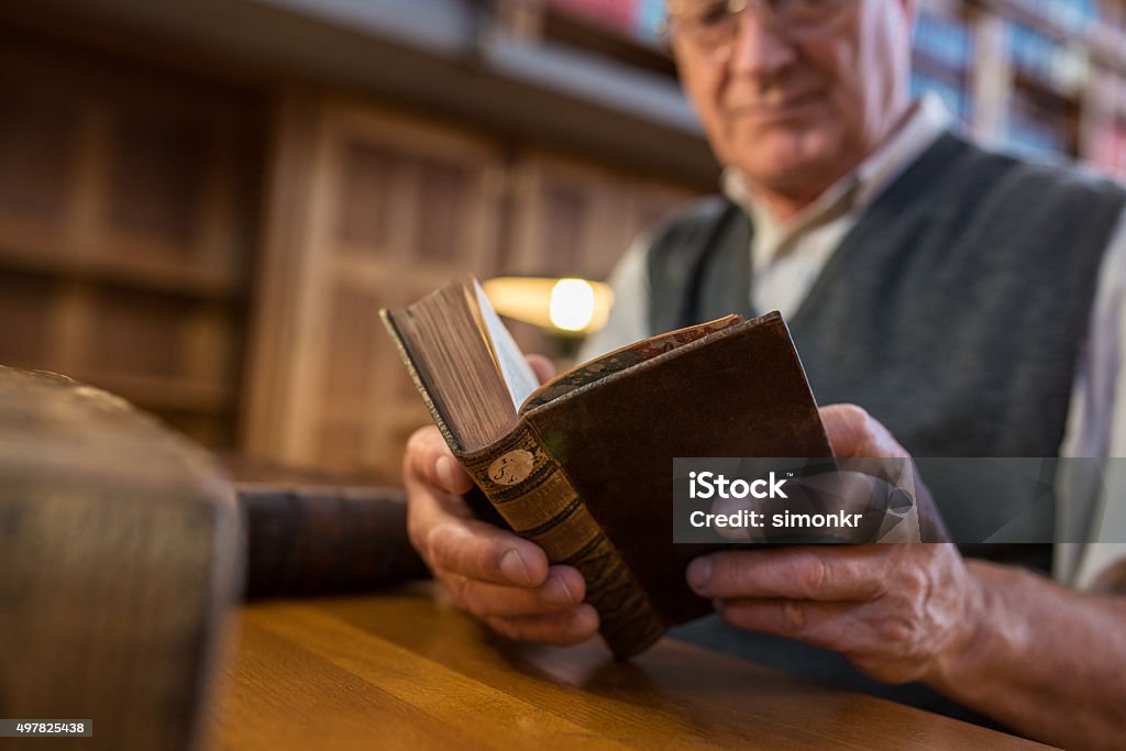 Senior man reading book Senior man sitting and reading book in library. Library Stock Photo