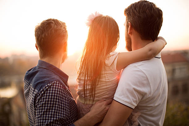 Gay Parents with daughter Young gay parents with their daughter having fun in park. Parents holding girl in arms. Enjoying in beautiful sunset. Caucasian ethnicity. surrogacy stock pictures, royalty-free photos & images