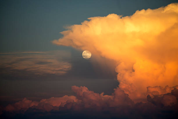 Full moon rising behind colourful clouds illuminated by the sunset